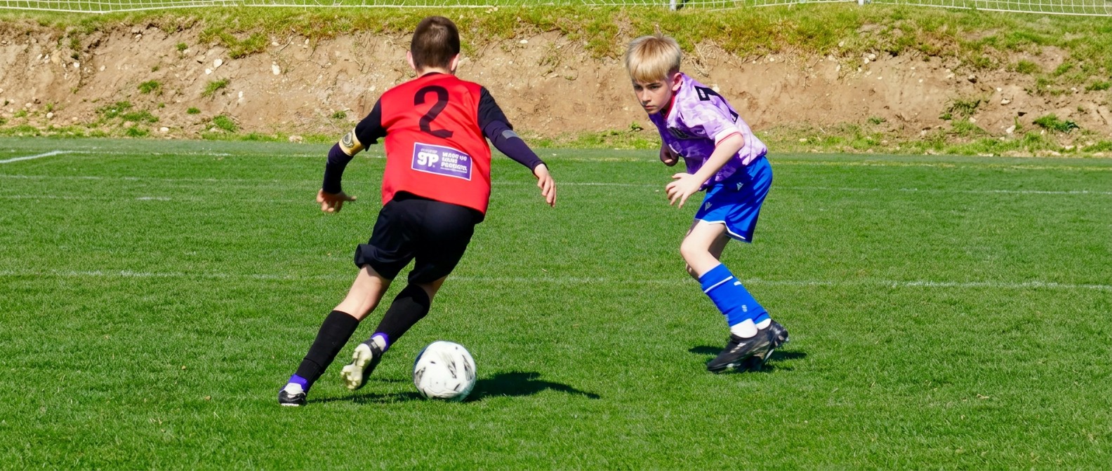 Junior players in red and purple competing during a football match in Alicante