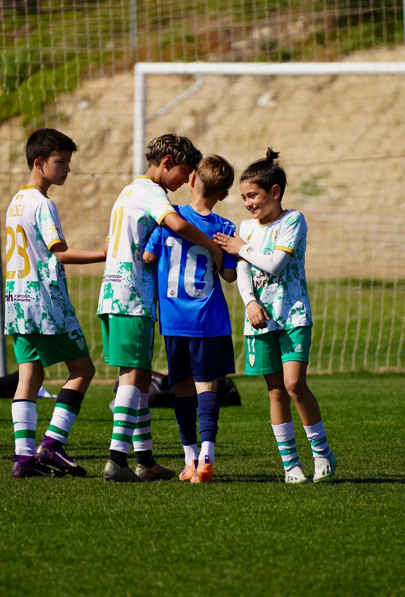 Junior players in white and blue showing sportsmanship during a football match in Alicante